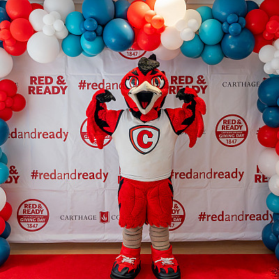 Carthage's Firebird mascot, Ember, poses in front of a wall decorated with Red and Ready decals and balloons.
