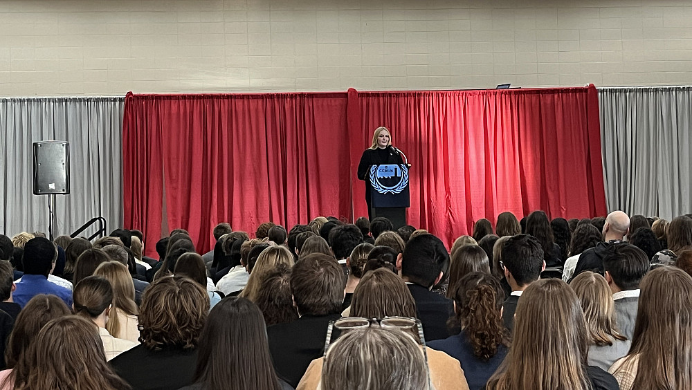 A student giving a speech at a podium on stage in front of an audience.