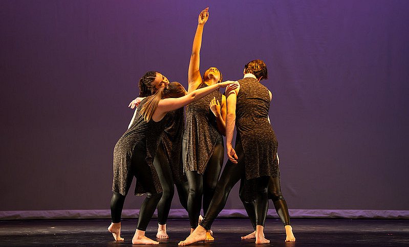 A group of female students in a huddle, performing on a dance stage.