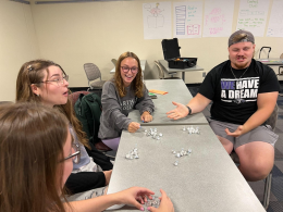 Students sitting at a gray table with small piles of Hershey kisses.
