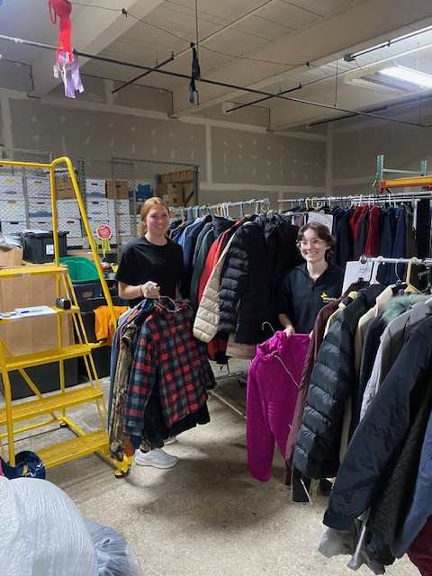 Two students organizing a rack of winter coats.