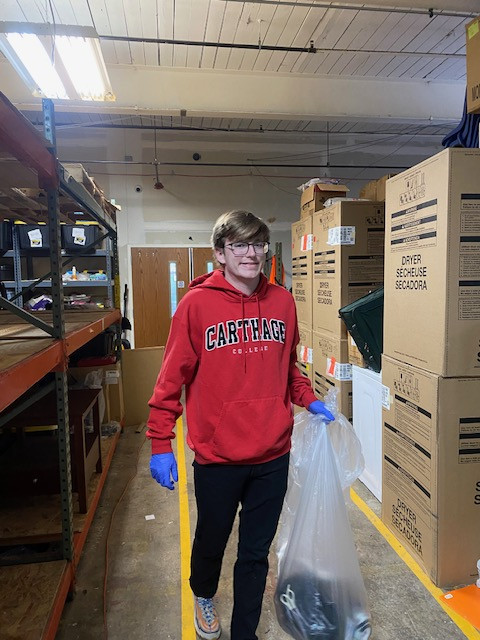 A student holding a garbage bag of winter clothes.