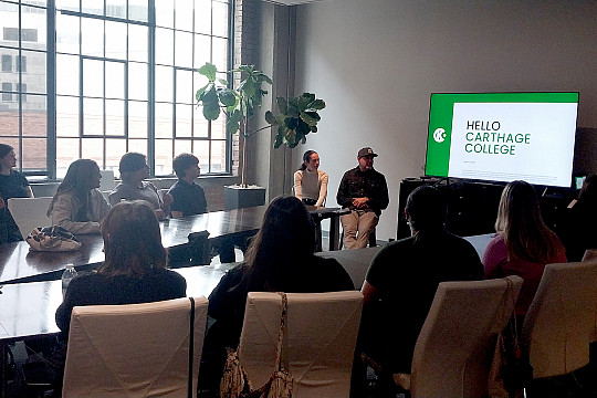 Students sitting at a table look at a presentation on a screen.