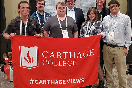 A group photo of the Carthage attendees and presenters in front of Nathan Cochran's poster. From left to right: Andy Huynh '25, Jerome Di...