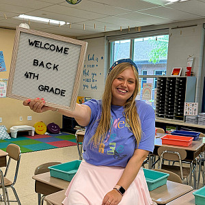 A teacher holding up a sign in an elementary school classroom.