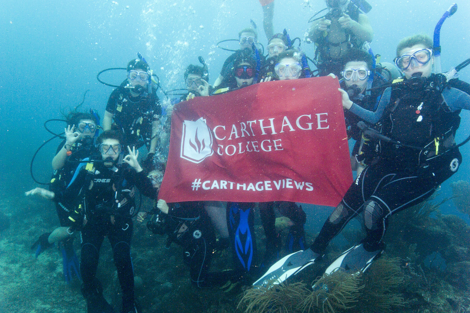 Students hold a Carthage flag while scuba diving on the J-Term study tour to Honduras.