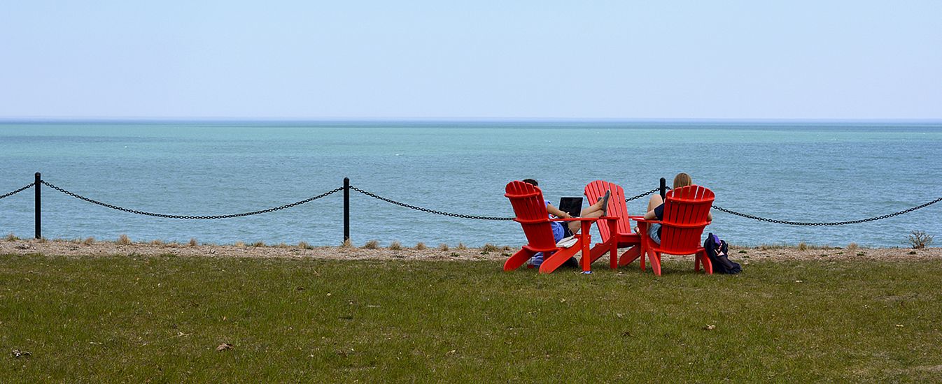 Two students unwind lakeside in Carthage's famous red adirondack chairs.
