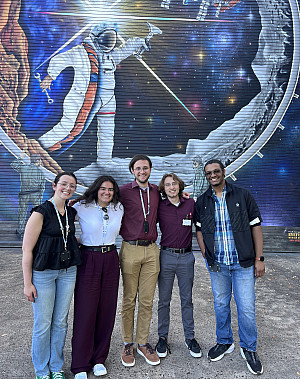 Students pose by a space-themed mural.